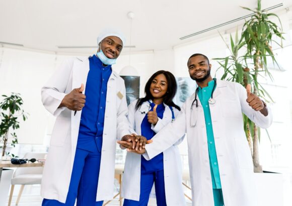 Doctors team. Health care. Three happy African doctors stack hands together as team for motivation