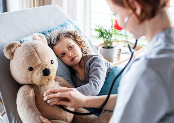 Friendly female doctor examining small girl in bed in hospital.